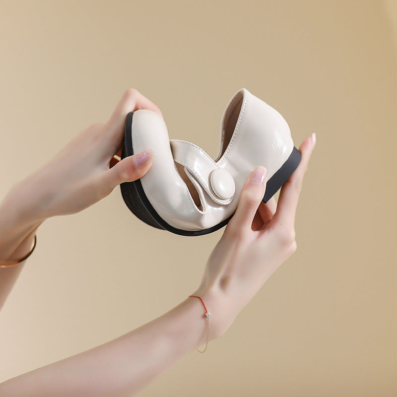 A pair of hands holding a beige Mary-Jane flat shoe, demonstrating its flexibility. The shoe features a strap with a round button detail.