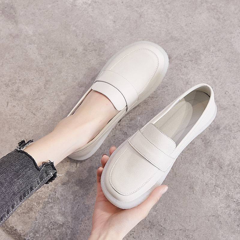 A pair of white slip-on casual loafers being demonstrated. One shoe is on a woman's foot, wearing frayed-edge denim pants, and the other is held by a hand on a gray textured surface.